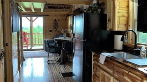 Interior de una cabaña de madera con cocina, comedor y vistas al exterior.