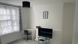 Una camera moderna e minimalista con una scrivania bianca, una sedia nera, un mobile TV in vetro e una lampada a sospensione.