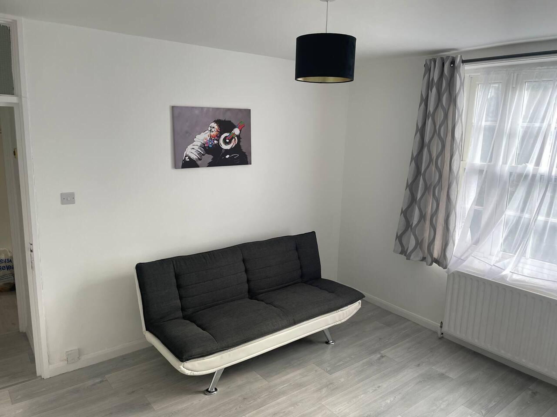 Un salon moderne avec un canapé gris, un luminaire suspendu, une fenêtre avec des rideaux légers et une œuvre d’art accrochée au mur.