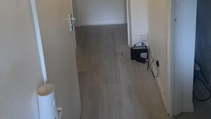 Un corridoio stretto con una porta in fondo, un lampadario sopra e una presa elettrica al muro.