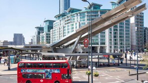Un autobus a due piani rosso a una fermata dell'autobus, con edifici moderni sullo sfondo.