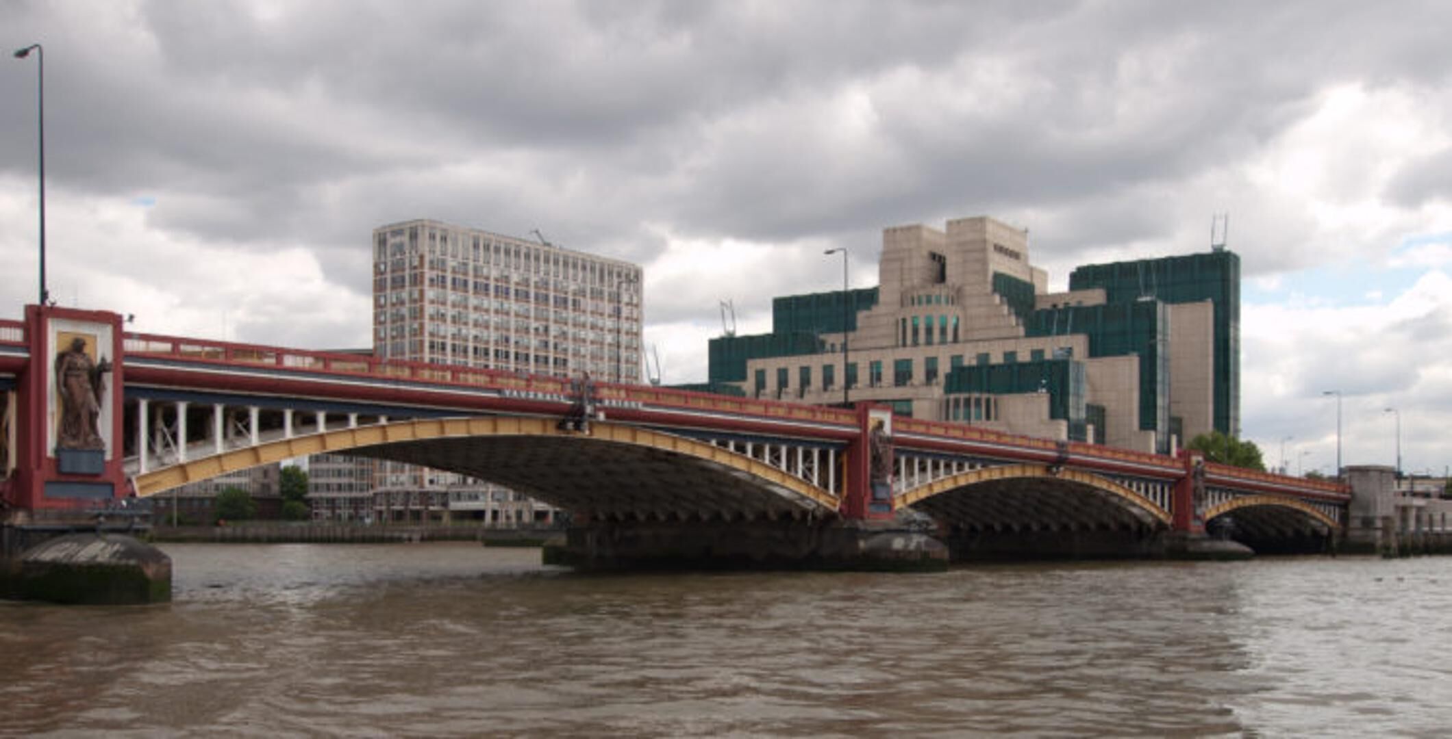 Un puente con una estatua a la izquierda, un edificio moderno con diseño único a la derecha, y un río en primer plano.