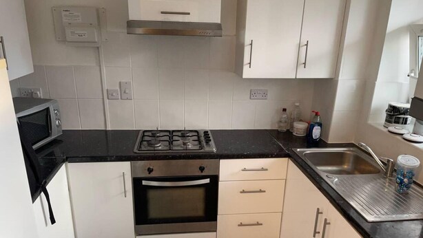 Una cucina moderna con mobili bianchi, un piano di lavoro nero, forno integrato, piano cottura a gas e lavello in acciaio inossidabile.