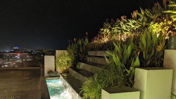A nighttime outdoor water feature with steps and plants, set against a cityscape. - Hotel Nyzote Inn (Dhaka)