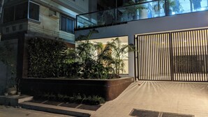 A modern building with a glass balcony, a gated entrance, and a landscaped area with plants. - Hotel Nyzote Inn (Dhaka)