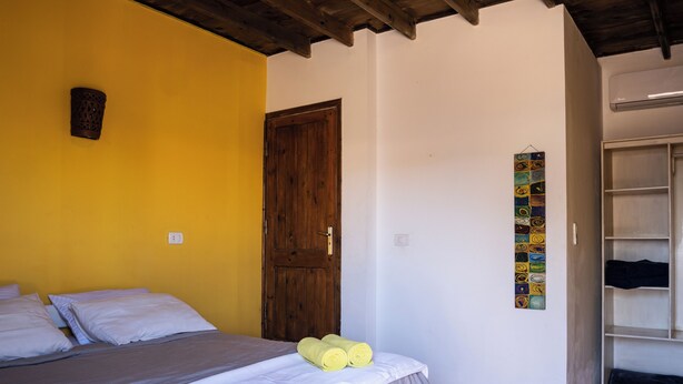 A bedroom with a bed, a wooden door, a wall with a colorful artwork, and a wardrobe. - Eldorado Lodge & Restaurant (Dahab)