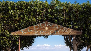 A wooden archway with the text "DORAL BEACH" leading to a sandy beach with a chair and a boat. - Eldorado Lodge & Restaurant (Dahab)