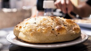 A round, golden-brown baked item on a white plate, possibly a bread or pastry, with a blurred background suggesting a dining setting. - Eldorado Lodge & Restaurant (Dahab)