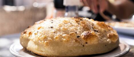 A round, golden-brown baked item on a white plate, possibly a bread or pastry, with a blurred background suggesting a dining setting.