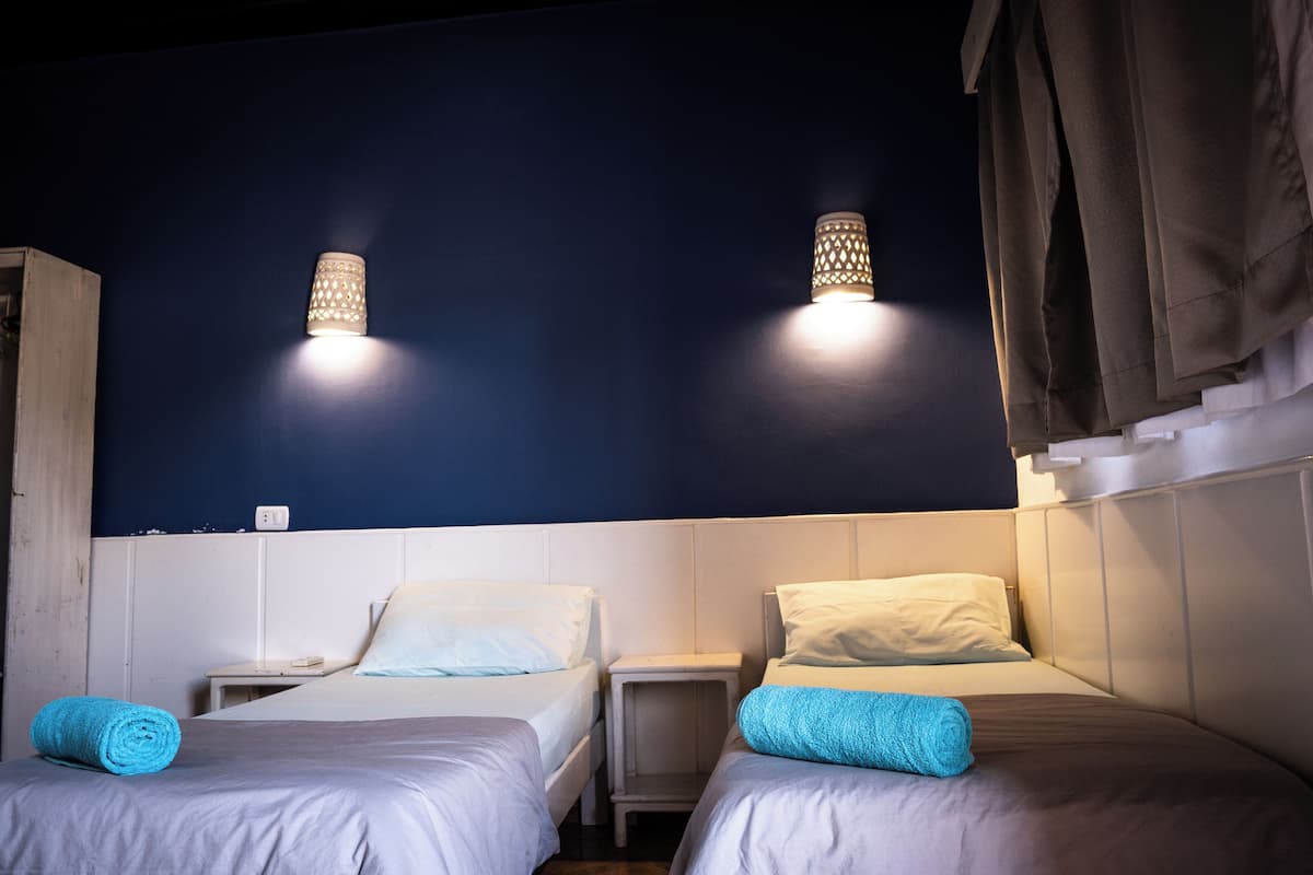 Una habitación con dos camas, una mesita de noche y una lámpara fijada a la pared.