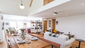 A spacious living area with a wooden dining table, a white sofa, and a bookshelf filled with books. - The Chapel (Alfreton)