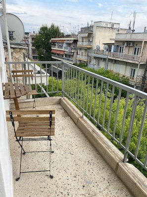 En balkong med en träbänk och ett metallräcke, med utsikt över ett bostadsområde med byggnader och grönska.