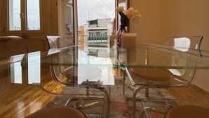 A modern dining area with a glass table and metal chairs, a vase of white flowers, and a view of buildings through a doorway. - Modern, Centrally Located Apartment (Thessaloniki)