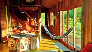 A wooden cabin interior with a dining area, a hammock, and a staircase leading to an upper level. - Pousada Sitio Gan Eden (Itatiaia)