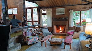 A cozy living room with a fireplace, comfortable seating, and a view of the outdoors. - Pousada Sitio Gan Eden (Itatiaia)