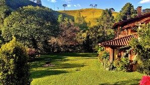 A wooden house with a red roof, surrounded by lush greenery and a well-maintained lawn. - Pousada Sitio Gan Eden (Itatiaia)