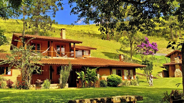 A two-story house with a tiled roof, surrounded by lush greenery and a hilly landscape. - Pousada Sitio Gan Eden (Itatiaia)