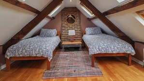 Une petite chambre mansardée, chaleureuse et accueillante, avec deux lits en bois, un tapis coloré tissé et un mur de briques agrémenté d’un miroir.