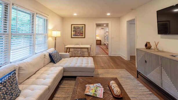 A modern living room with a sofa, ottoman, coffee table, and a TV mounted on the wall. - 4 BR Sleeps 10 Near UGA & Downtown (Athens)