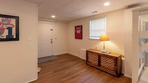 A hallway with wooden flooring, a white door, a framed picture, a wooden cabinet with a lamp, and a window with blinds. - 4 BR Sleeps 10 Near UGA & Downtown (Athens)