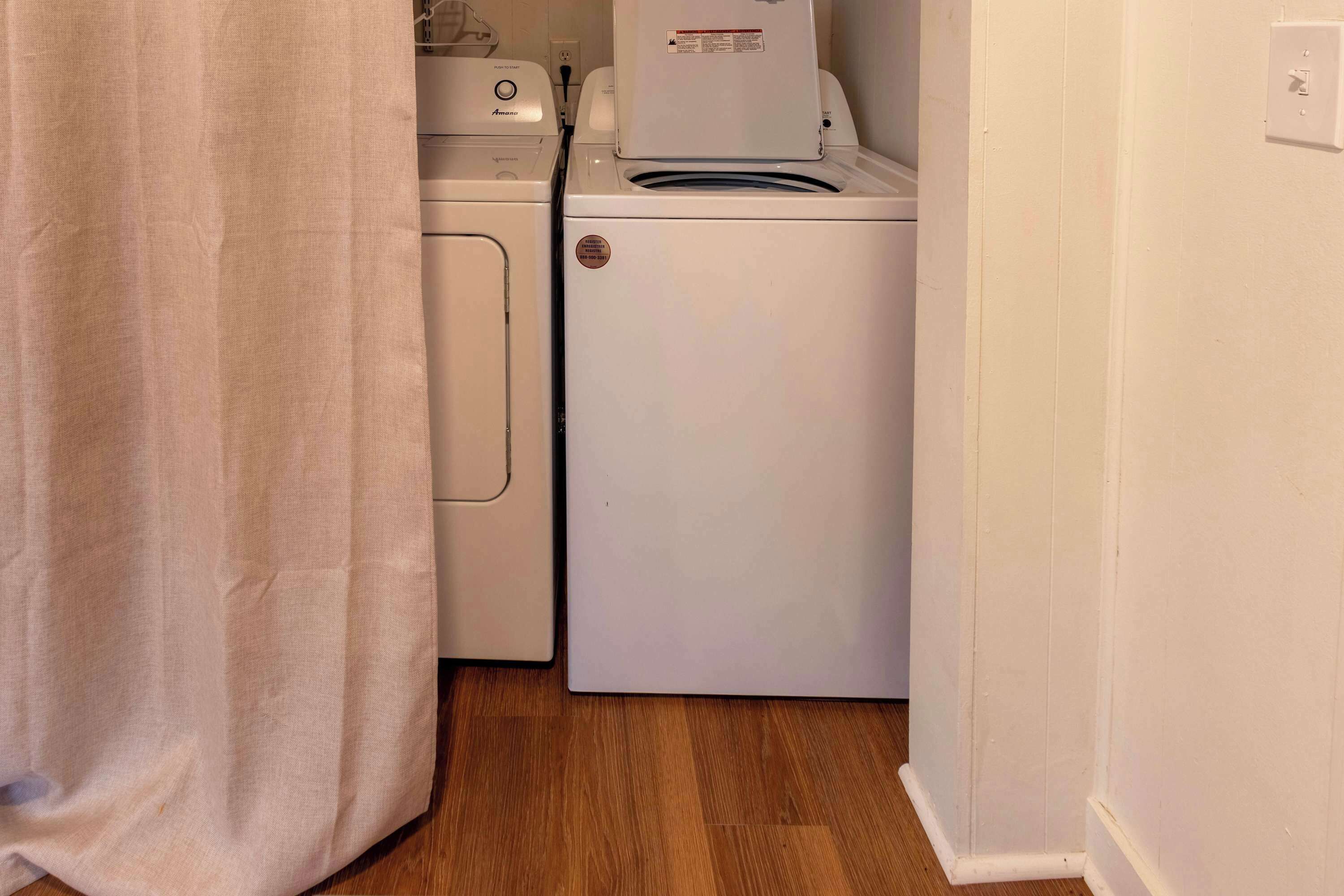 A laundry area with a front-loading washer and dryer, wooden flooring, and a white wall.