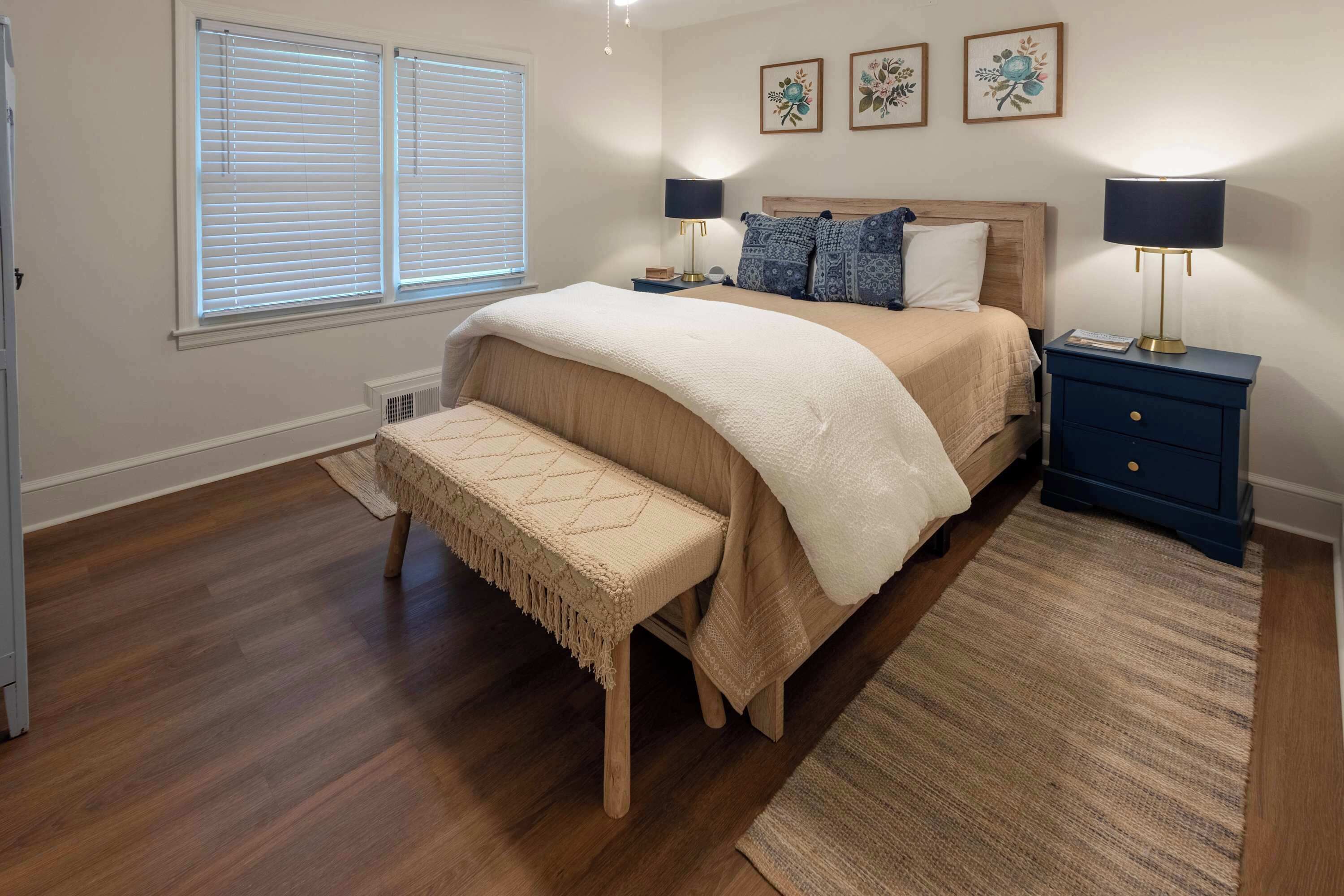 A bedroom with a bed, bench, bedside tables, lamps, and framed artwork on the wall.