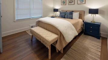 A bedroom with a bed, bench, bedside tables, lamps, and framed artwork on the wall.
