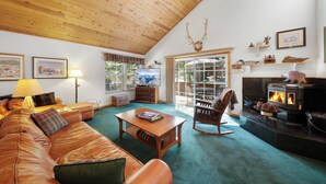 A cozy living room with a wooden ceiling, a leather sofa, a coffee table, a rocking chair, a fireplace, and a television.