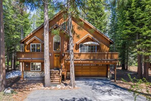 A two-story log cabin with a stone foundation, a garage, and a covered porch. - Paradise Pines 3BR Secluded Cabin Minutes in Tahoe Donner! (Truckee)