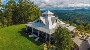 A large, white, metal-roofed house with a prominent tower, surrounded by lush greenery and a mountainous backdrop. - 6BD, 5 Bath - Mountaintop Mansion in the Sky (Tellico Plains)