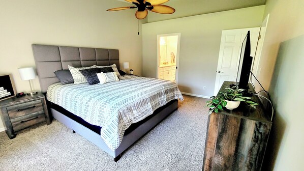 A bedroom with a bed, nightstands, a dresser, a ceiling fan, and a door.