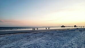 Een strand met een pier en mensen die langs de kust wandelen.