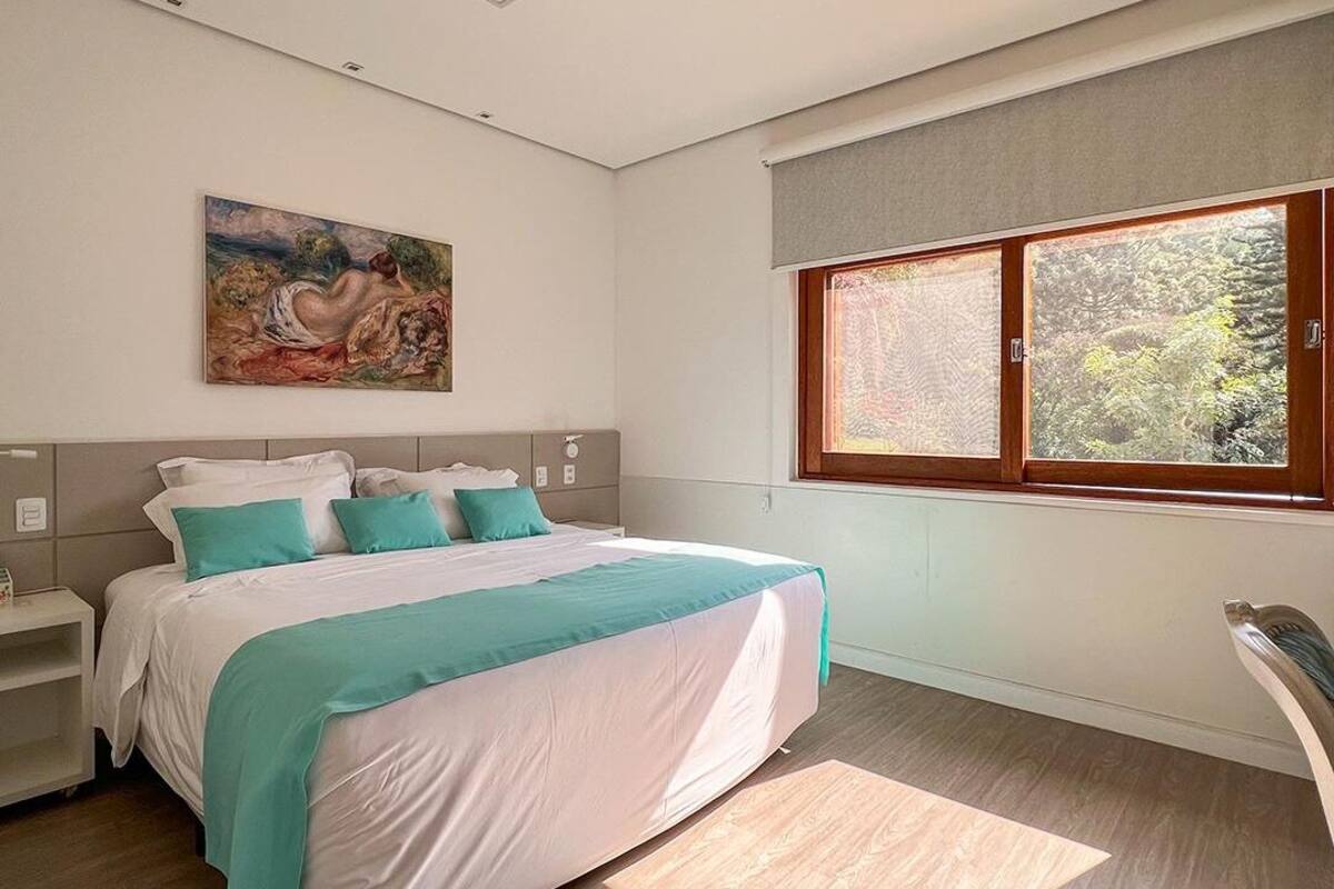 A modern bedroom with a large bed, a painting on the wall, and a window with a view of trees.