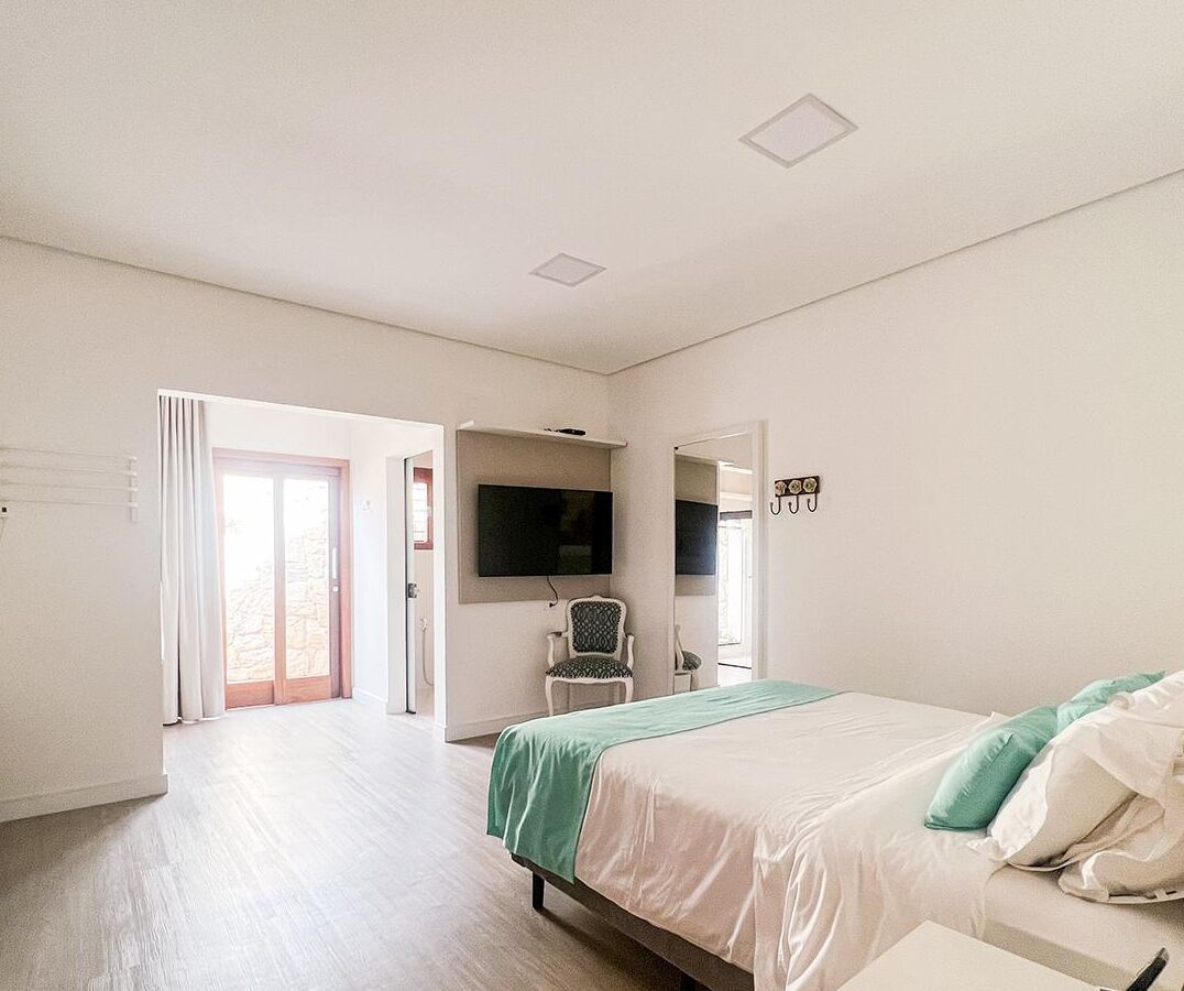 Una habitación de hotel con cama, una silla, televisor montado en la pared y una puerta corrediza de vidrio que da a un espacio exterior.
