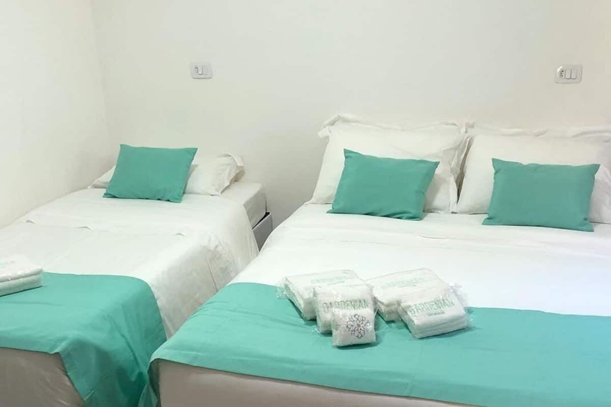 Two single beds with white bedding and teal pillows, each with a neatly folded towel on the bed.