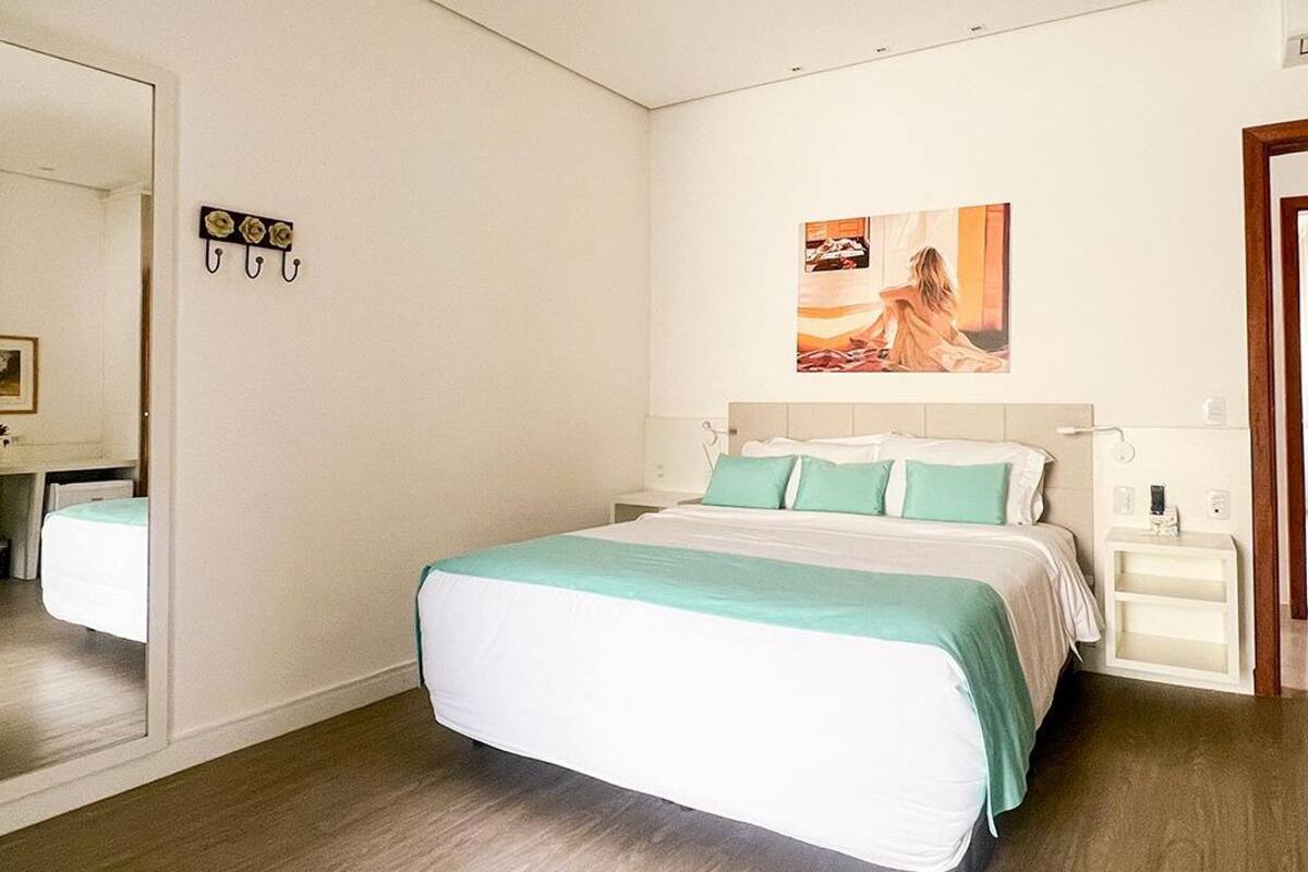A hotel room with a large bed, a nightstand, a mirror, and a painting on the wall.