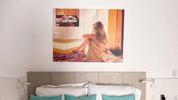 Quarto com cama, almofadas azul-turquesa, mesa de cabeceira e um quadro na parede.