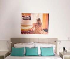 Quarto com cama, almofadas azul-turquesa, mesa de cabeceira e um quadro na parede.