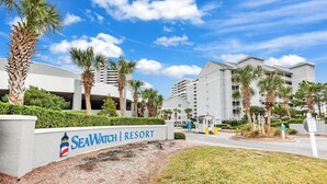 A resort entrance with a sign reading "SeaWatch Resort," palm trees, and modern buildings in the background. - Oceanfront Updated Condo at SeaWatch Resort 6 Pools 10 Hot Tubs Balcony King Bed (Myrtle Beach)