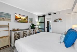 A modern bedroom with a large bed, a wooden sideboard, and artwork on the walls.