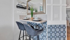 A kitchen with a white countertop, two bar stools, a mirror, and a backsplash with blue and white tiles. - Oceanfront Updated Condo at SeaWatch Resort 6 Pools 10 Hot Tubs Balcony King Bed (Myrtle Beach)