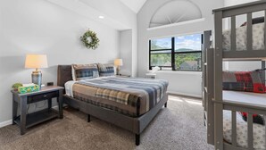 Un dormitorio con cama, mesitas de noche, escritorio, ventana con vistas y literas.