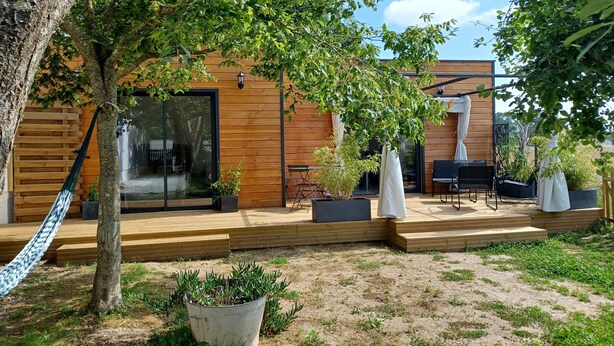 Un espace extérieur moderne avec une terrasse en bois, un hamac et des plantes en pot.