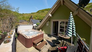 A cozy outdoor area with a hot tub, wooden benches, a table with an umbrella, and a chair.