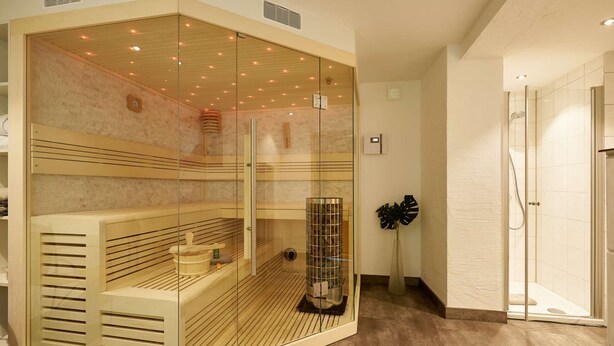 A sauna with a wooden bench, glass walls, and a tiled floor.
