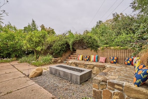 A garden with a fire pit, stone seating, and colorful cushions.
