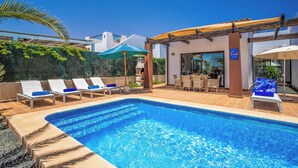 Piscina con sillones de descanso, un área de estar techada y vista a un edificio moderno.