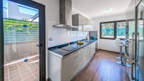 Una cocina moderna con una isla grande, electrodomésticos de acero inoxidable y vistas a un jardín verde a través de un ventanal.