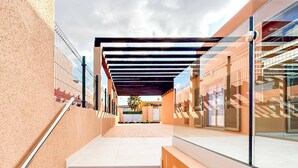 Un bâtiment moderne doté d’une façade en verre, d’un espace extérieur couvert et d’un escalier menant à l’entrée.