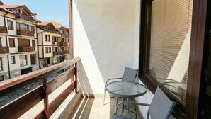 A balcony with a glass table and chairs, a wooden railing, and a view of multi-story buildings. - Mountain Paradise 2 - Quiet Cosy Studio - Balcony, Wifi (Bansko)